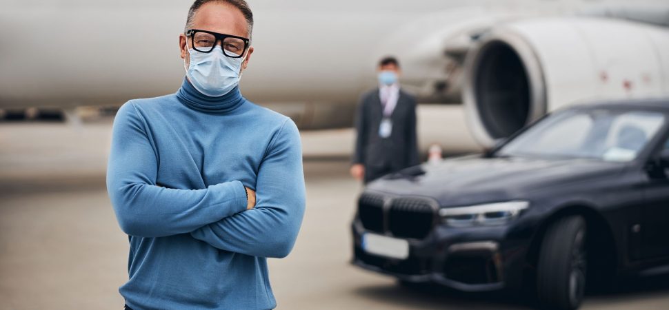 Male entrepreneur standing on the runway in front of the car and an airport worker